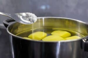 shutterstock 2486876055 A pot of water with peeled potatoes and a spoon dumping in salt