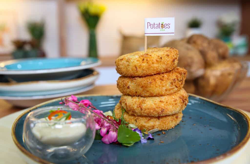 U.S. Mashed Potato Crabcakes stacked on top of a plate with flower garnish and a dipping sauce