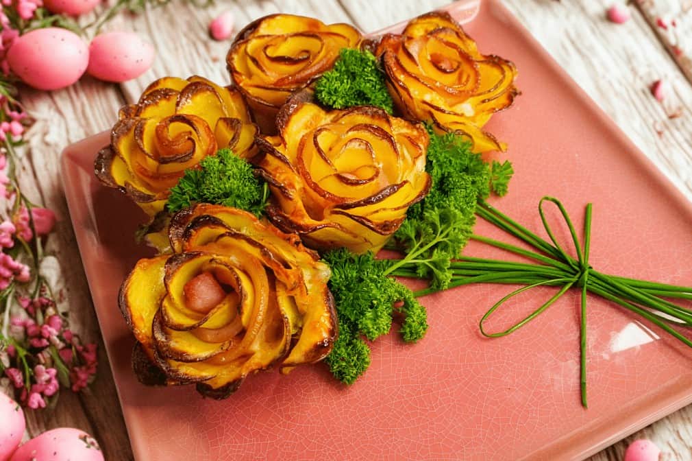 Potato Roses Five potato slices arranged as rose flowers on a pink plate, garnished with parsley and chives tied to look like flower stems; pink decorative eggs and flowers surround the plate.